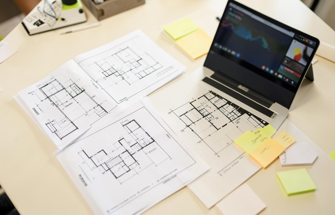 Planning table with printed system diagrams, notes, and a laptop showing a dashboard
