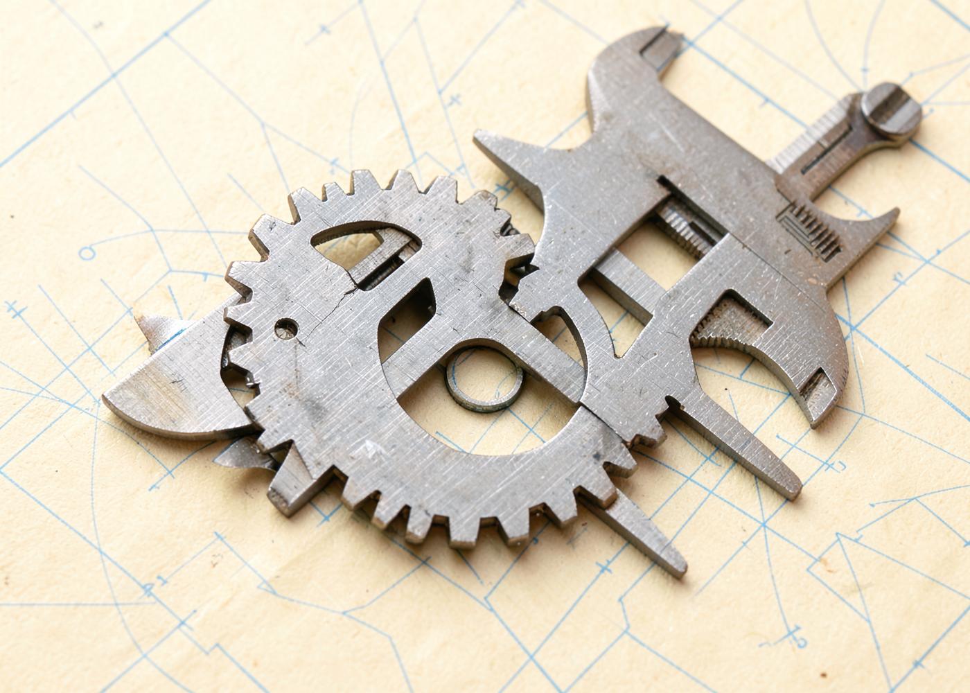 Precision engineering tools and gears resting on paper marked with blueprint grid lines